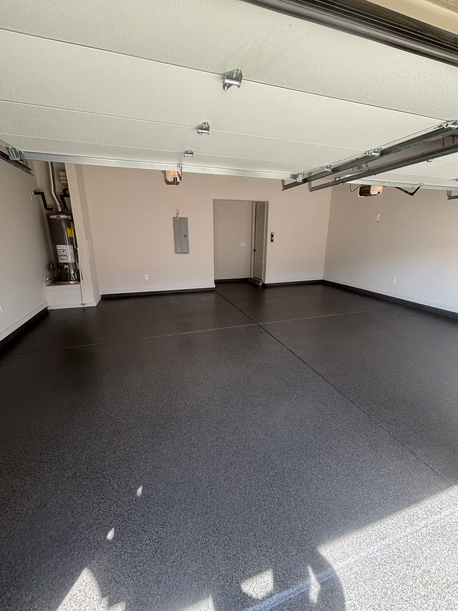 Two-car garage with a charcoal flake floor, water heater in the corner