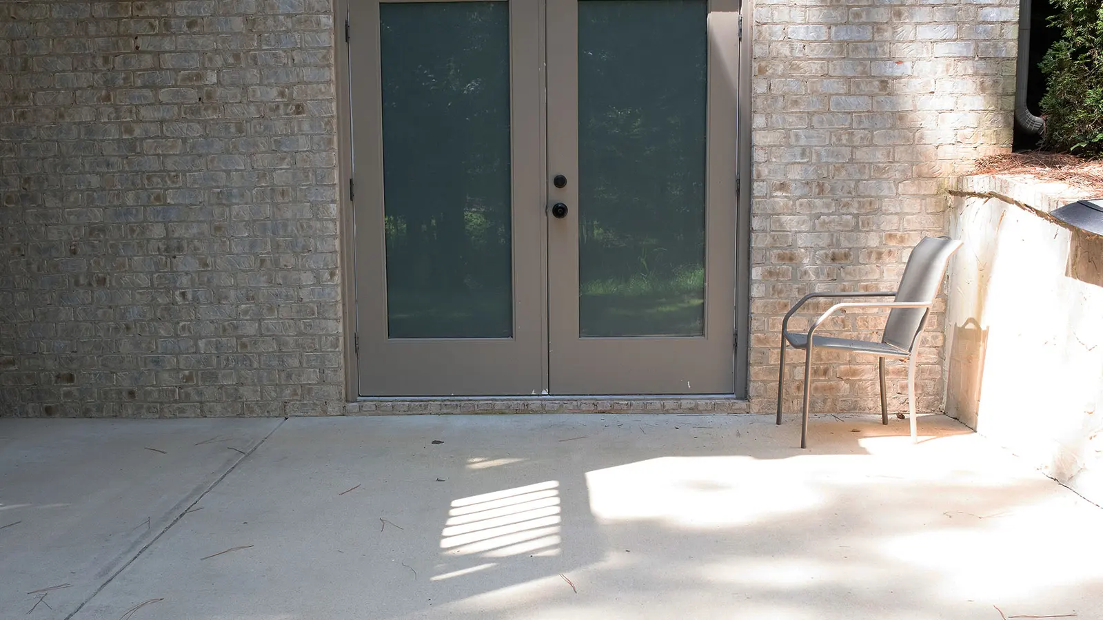 Bare concrete patio outside a set of french doors, stained and dusty