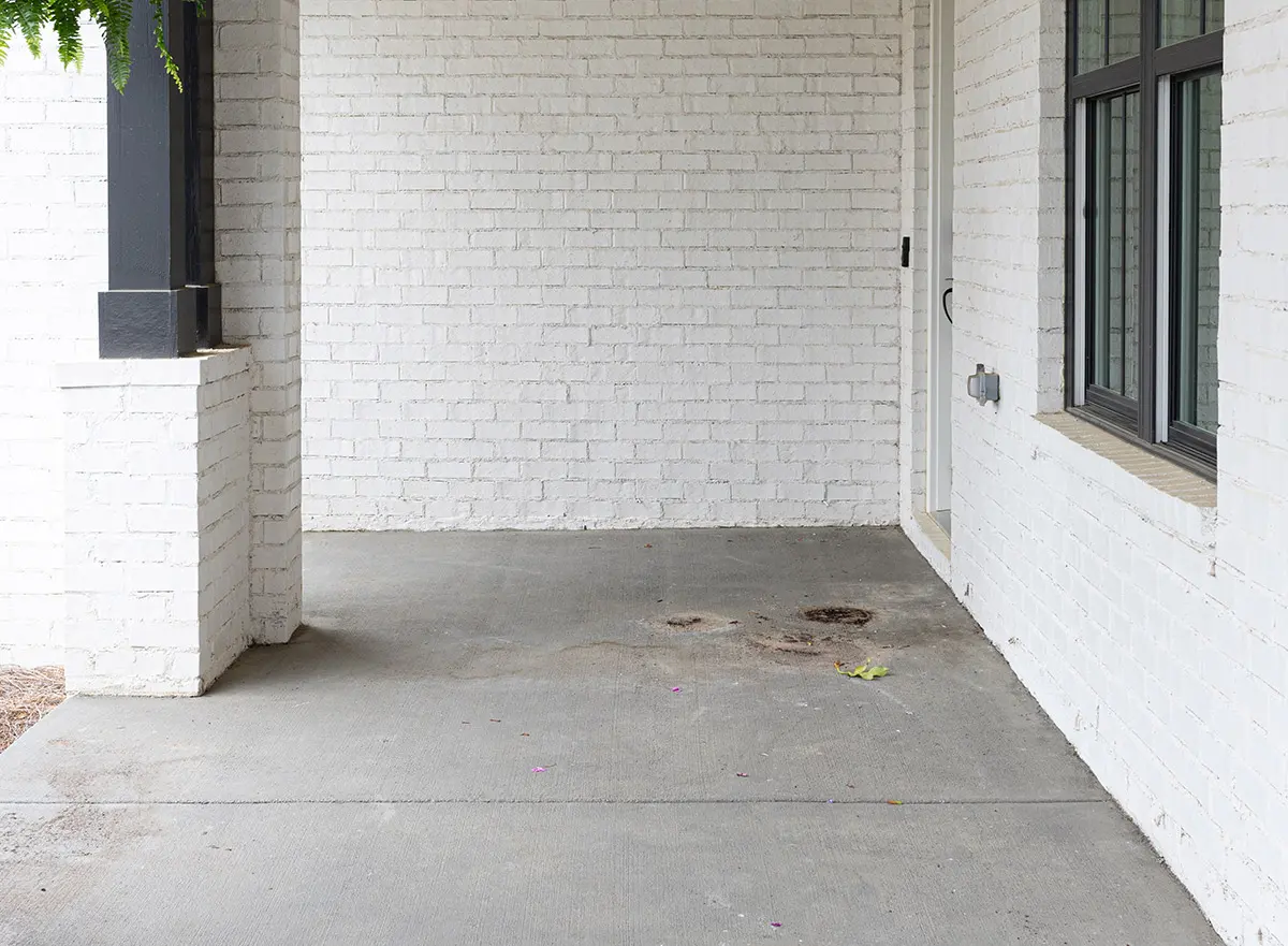Covered porch with a stained bare concrete slab against white brick